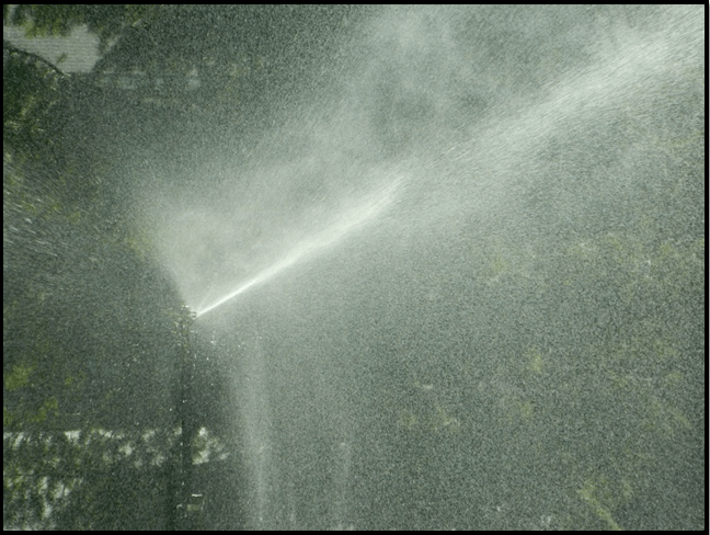 Photo Showing Ground Sprinkler Misting The Air.  Firehawk Sprinkler Mid Stream Of Water And Adjusted To Misting For Full Mist To Cool The air.  Also Operates In Full 360 Degrees Radius And Is Adjustable to 180 Degrees, Down to 90 Degrees, And Down to 20 Degrees.